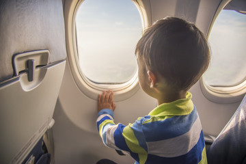 Obraz premium azjatycki chłopiec patrząc z lotu ptaka niebo i chmura na zewnątrz okna samolotu, siedząc na siedzeniu samolotu.
