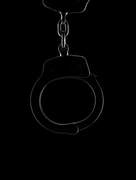 Backlit handcuff silhouette on a black background with copy space below handcuffs