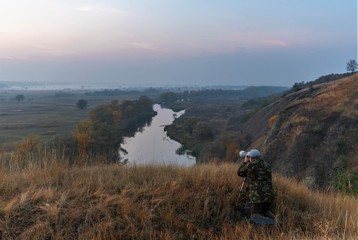 the photographer is shooting the autumn landscape with the sunrise by the river