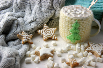 Christmas composition. Hot cocoa with marshmallows in knitted Cup, scattered ginger cookies in glaze on a white background