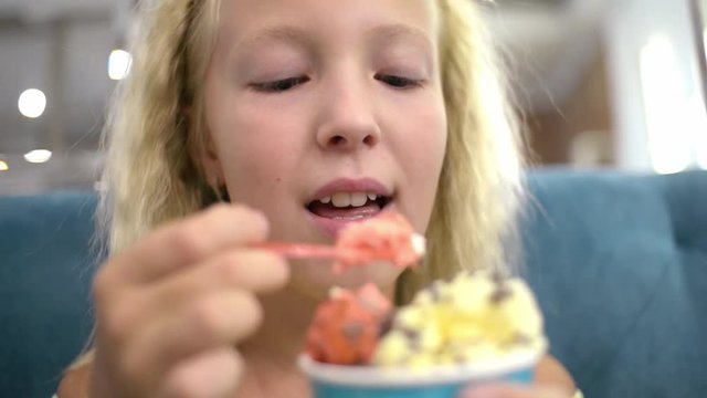 Girl Blonde eat fruity Ice cream Dessert with Spoon sitting by cafe Table