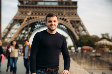 A young man wearing a dark blue jacket is standing on the background of the Eiffel Tower. Sunny...