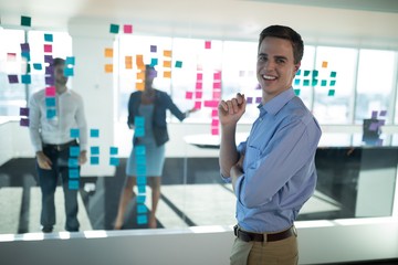 Male executive standing in office with colleagues in background