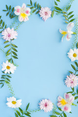Frame of chamomiles, branches, leaves and lilac petals on blue background. Flat lay, top view