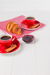 Freshly baked croissant on napkin, cup of coffee in red cup on white wooden background. French breakfast. Fresh pastries for breakfast. Delicious dessert. Closeup photography. Vertical banner