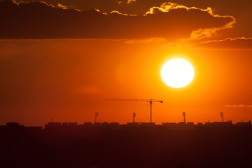 Twilight over the city of Bucharest. Construction crane, building silhouettes and sun circle in the background