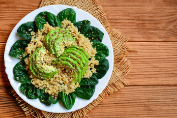 Quinoa avocado spinach salad. Simple quinoa salad with fresh spinach and avocado slices on a served plate. Brown wooden background with copy space for text. Top view