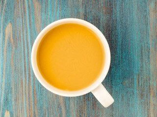 large white mug of tea with milk on a wooden blue background, a traditional English drink.