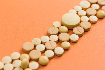 Heap of assorted beige capsules on orange table.