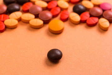 Heap of assorted brown, orange and red capsules on orange table. One pill is apart, isolated.