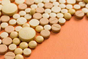 Fototapeta na wymiar Heap of assorted beige capsules on orange table.
