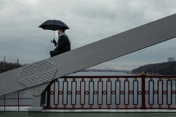 lonely man with umbrella sitting on bridge construction