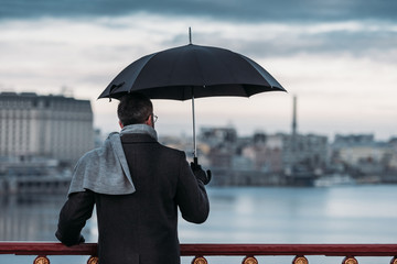 back view of lonely man with umbrella standing on bridge