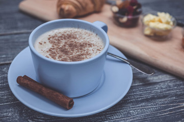 Croissant, orange jam, butter and coffee with milk and cinnamon. Continental breakfast concept. Wooden background
