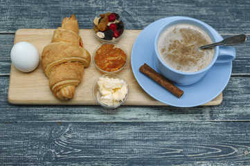 Croissant, orange jam, butter and coffee with milk and cinnamon. Continental breakfast concept. Wooden background
