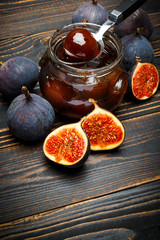 Glass jars full of fig jam and fig fruits on a dark wooden background