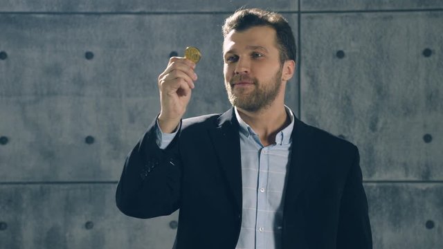 Smiling man looks at bitcoin in his hand and puts it on pocket