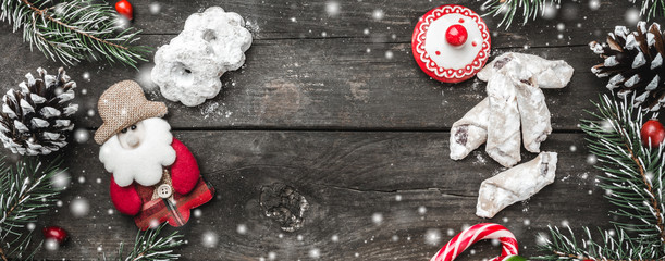 Panoramic Christmas theme with fir branches, snowman handmade toy, cones, cookies and candies, on rustic dark wooden background viewed from above, top, in snow greeting card with space for text