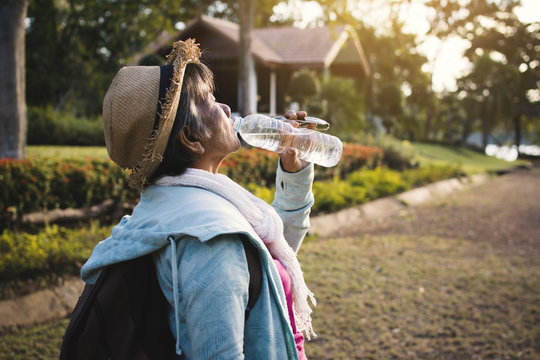Happy hipster old women drinking water of bottle during backpack traveling on the road relax time in holiday, color vintage style selective and soft focus