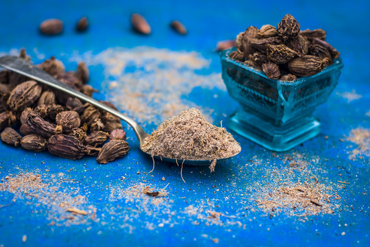 Raw black cardamom on a bluish surface with its powder.;
