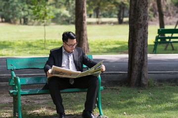 Businessman sitting on bench in the Park. looking read newspaper. Concept Relaxing Working