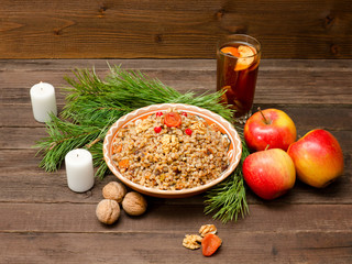 Dish of traditional Slavic treat on Christmas Eve. Pine branches, candles, apples, walnuts, glass of compote. Brown wooden background.