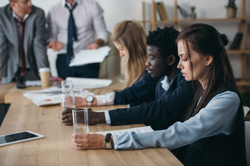 group of managers sitting with glasses of water in conference hall at office