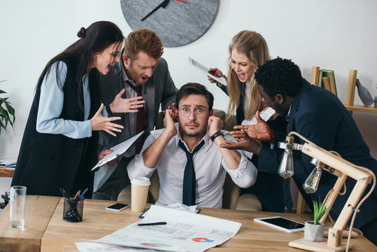 businessman having trouble with deadline and covering ears while colleagues shouting at him