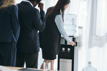 businesspeople standing in queue for water dispenser at office