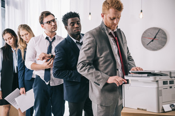 group of young managers standing in queue for copier at office