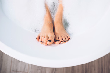 Well groomed woman's legs in bath foam close up image