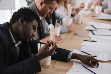 exhausted african american businessman eating noodles with his colleagues at office