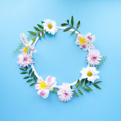 Frame of chamomiles, branches, leaves and lilac petals on blue background. Flat lay, top view