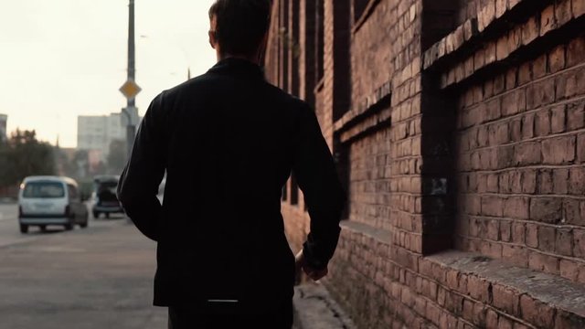 Slow motion sportsman running along old street. Young free determined professional runner morning workout. Back view