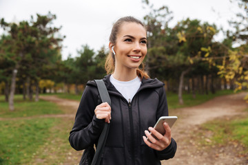 Portrait of a smiling sportsgirl in earphones holding mobile phone
