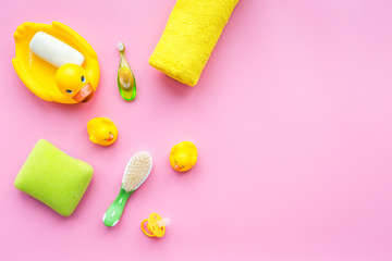 Bath accessories for kids. Yellow rubber duck, soap, sponge, brushes, towel on pink background top view copyspace