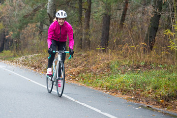Fototapeta na wymiar Young Woman in Pink Jacket Riding Road Bicycle in the Park in the Cold Autumn Day. Healthy Lifestyle.