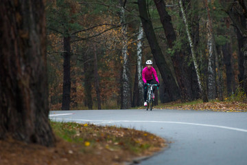 Obraz premium Young Woman in Pink Jacket Riding Road Bicycle in the Park in the Cold Autumn Day. Healthy Lifestyle.