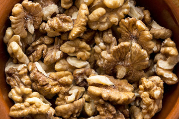 a lot of natural walnuts in a brown ceramic bowl on a white background