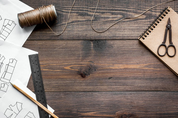 Tailor's work desk. Pattern of clothing and tools on dark wooden background top view copyspace