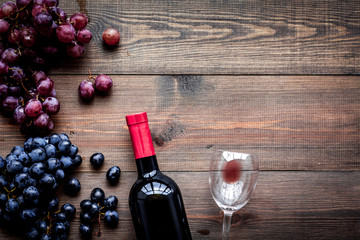 Taste red wine. Bottle of red wine, glass and black grape on dark wooden background top view...