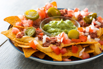 Mexican nachos with beef, guacamole, cheese sauce, peppers, tomato and onion in plate on wooden table

