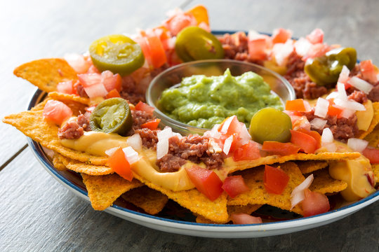Mexican nachos with beef, guacamole, cheese sauce, peppers, tomato and onion in plate on wooden table

