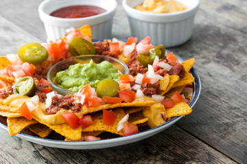 Mexican nachos with beef, guacamole, cheese sauce, peppers, tomato and onion in plate on wooden table

