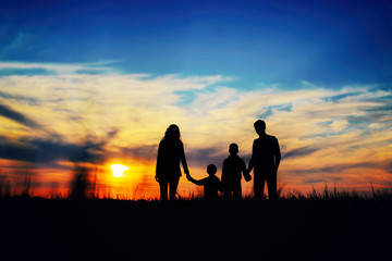 Fototapeta na wymiar Father, mother, and children hold hands on a sunset background.
