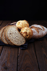 Different kinds of bread and bread rolls on brown wooden table. Kitchen or bakery poster design.