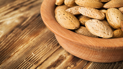 Almond in shells in wooden plate on rustic old table. Raw food ingredients