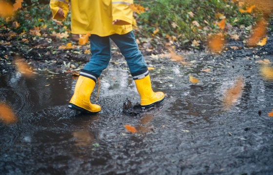 Child With Yellow Rain Boots Playing Outdoors In An Autumn Forest Jumping In Puddles Enjoying Nature With Falling Leaves