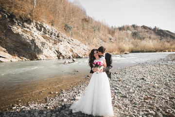 Fototapeta na wymiar Beautifull wedding couple kissing and embracing near the shore of a mountain river with stones