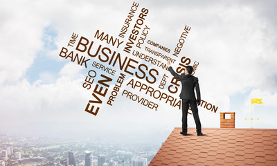Young businessman standing on house roof and writing leadership skill concept. Mixed media